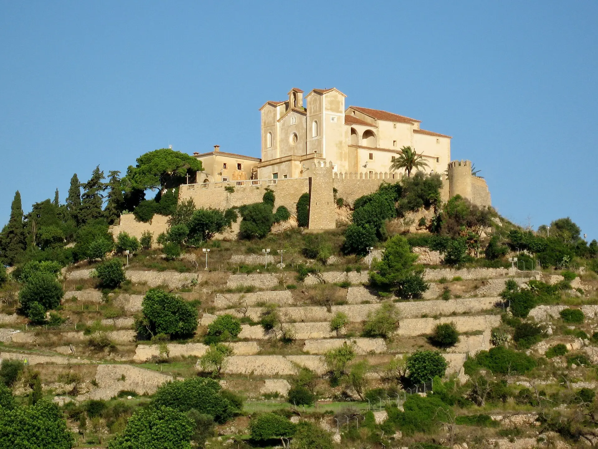 The sanctuary of Sant Salvador above the terraced walls of Artà in evening light