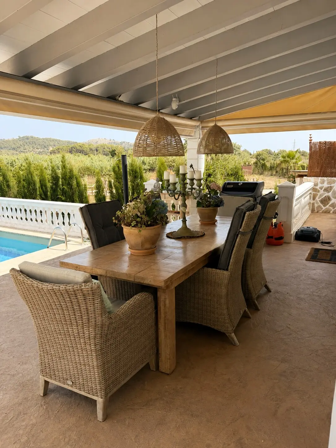 Covered outdoor dining area with wicker pendants and a view across the land
