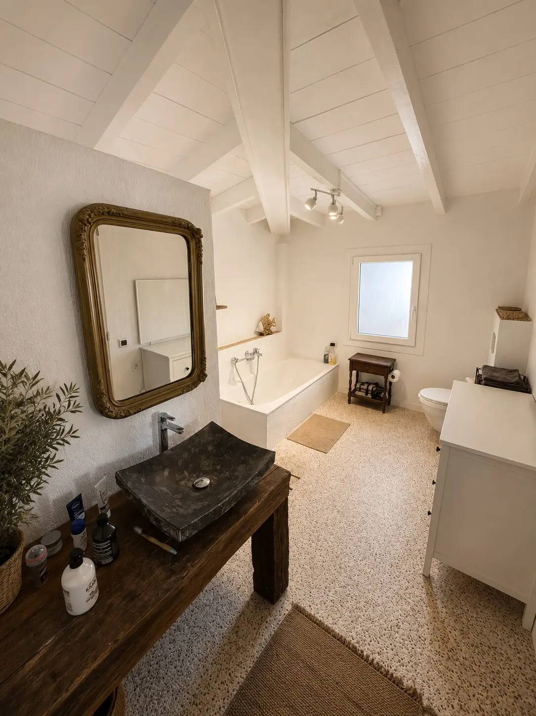 Bathroom with a stone basin on a wooden console, bathtub and white-painted ceiling