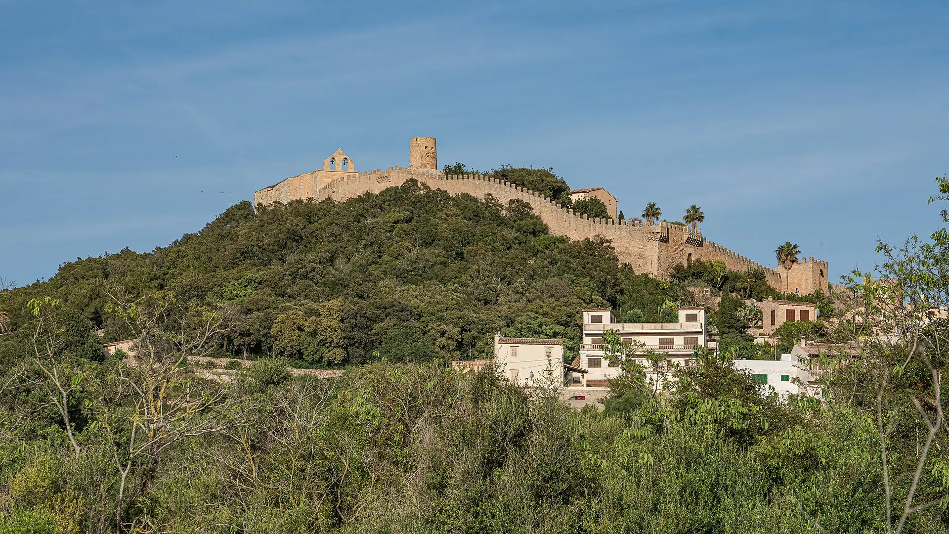 The Castell de Capdepera with its crenellated wall above the wooded hill, the town's houses below