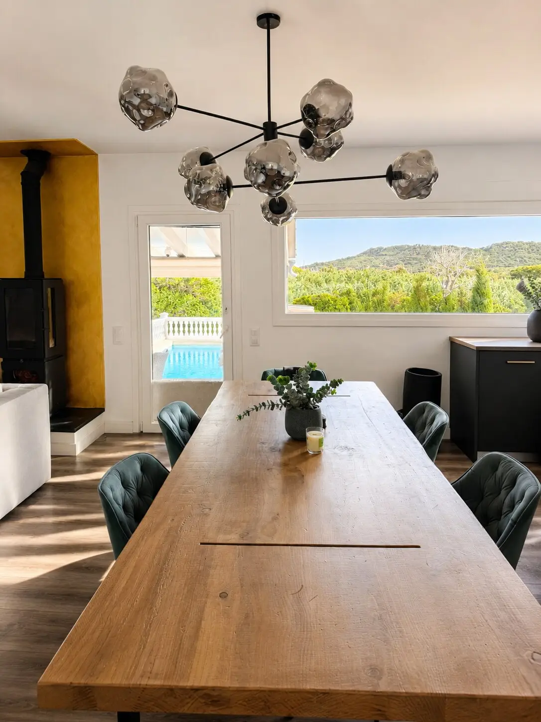 Dining area with a long wooden table, designer pendant and a view to the pool