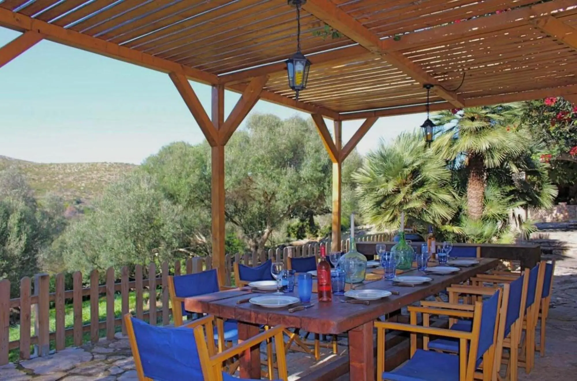 Long dining table under the timber pergola, looking out over olive trees and hills