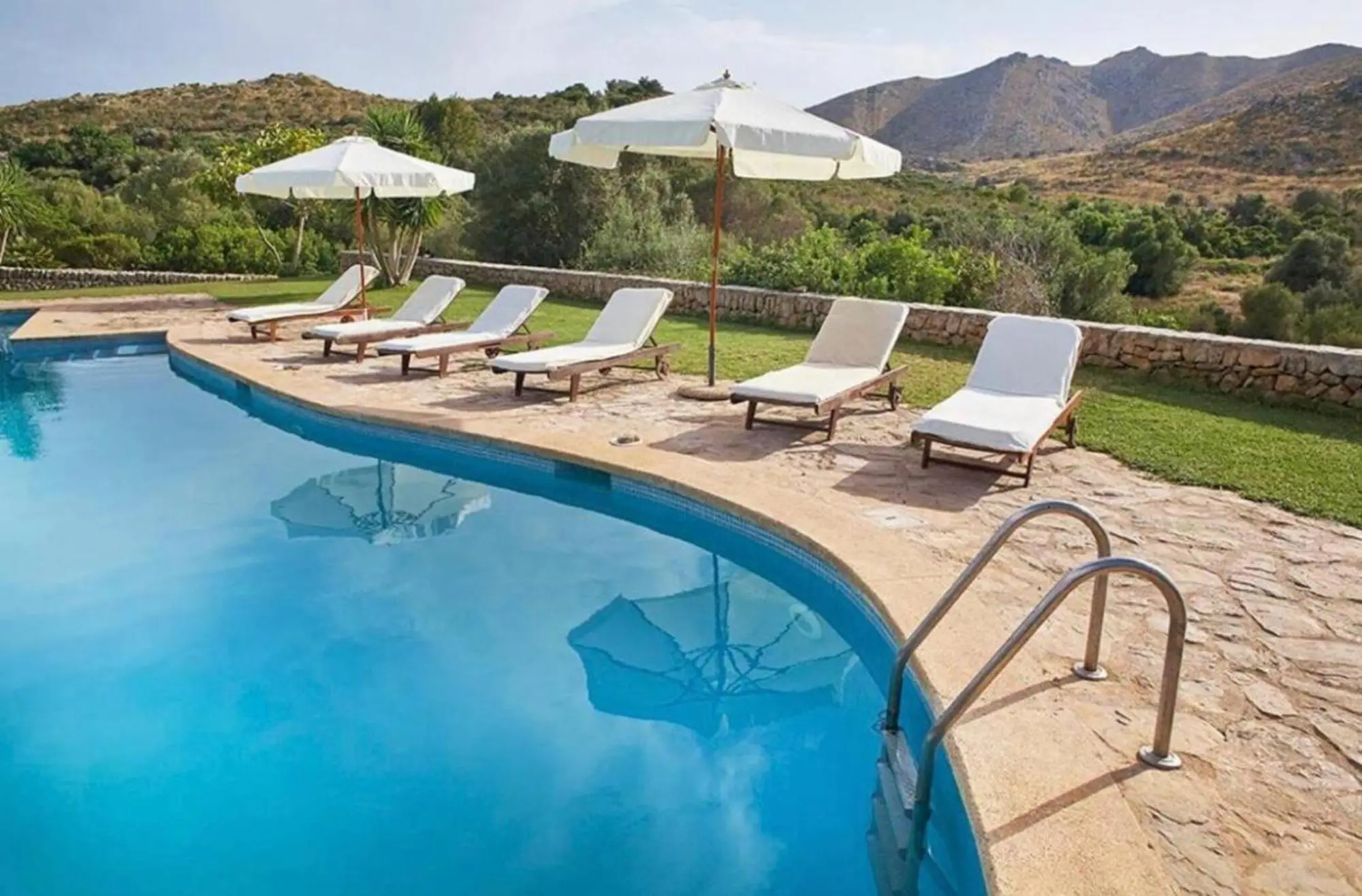 Pool with loungers and parasols, the hills of the Serra de Llevant behind