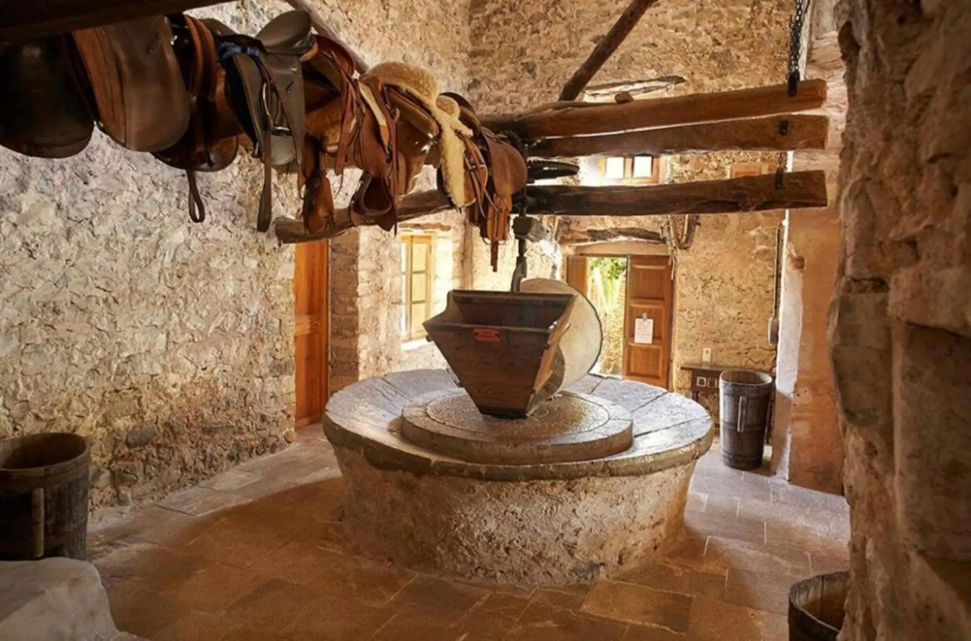 Millstone of the historic tafona under the ceiling beam, saddles hanging above